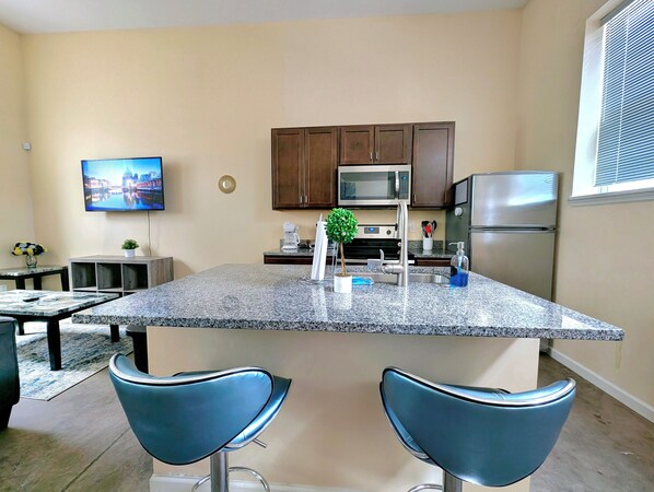 A kitchen with granite countertops, stainless steel appliances, and two blue bar stools.