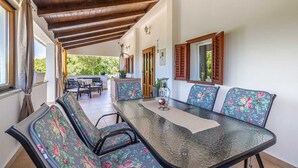 A dining area with a glass-top table, floral upholstered chairs, wooden beams on the ceiling, and a view of greenery outside. - Holiday house CHARMING with private pool (Kras)