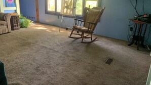 A room with a rocking chair, a small table with a television, and a window with blinds.