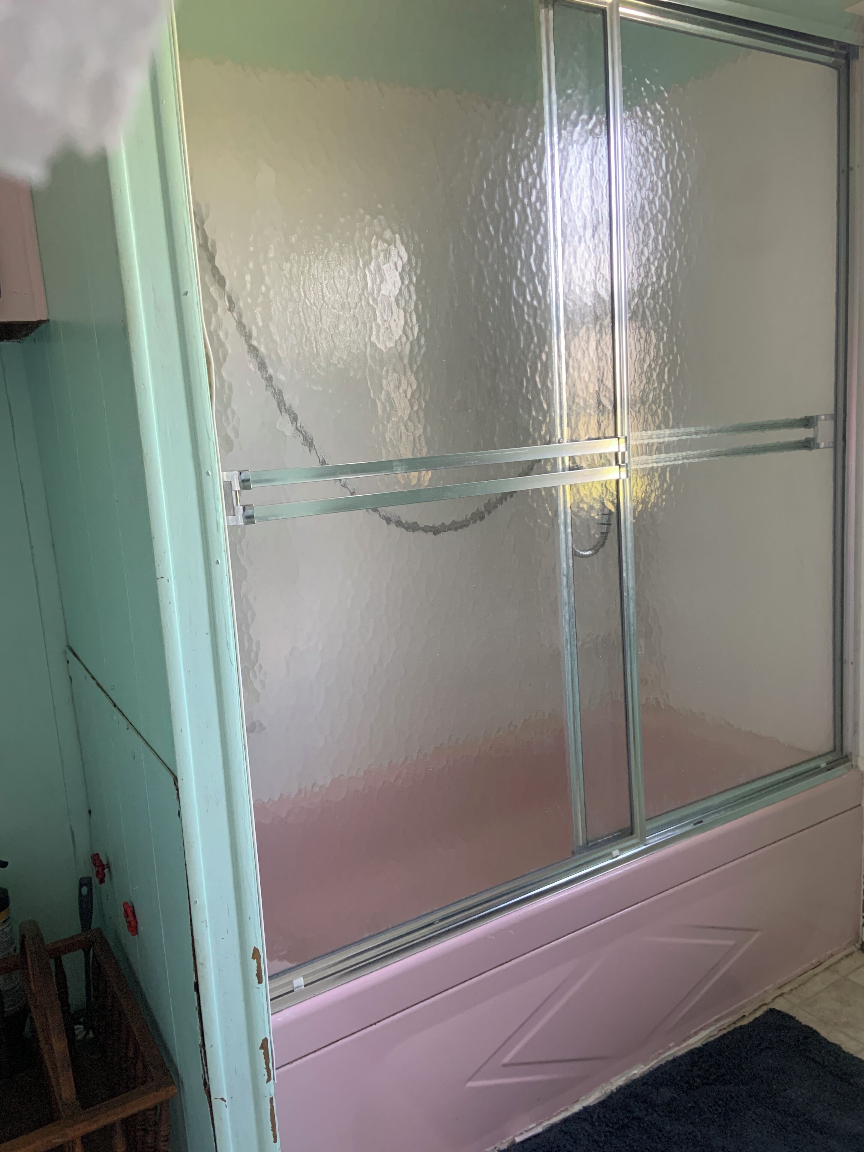Une salle de bain avec une douche à parois de verre, un meuble-lavabo rose et un tabouret en bois.