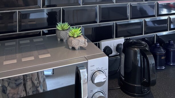 A kitchen with a black tiled backsplash, a stainless steel range hood, a coffee maker, and a small potted plant. - Cozy and modern studio in prime location-perfect for your getaway (Brighton and Hove)