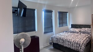A bedroom with a bed, a TV mounted on the wall, and a standing fan. - Cozy and modern studio in prime location-perfect for your getaway (Brighton and Hove)