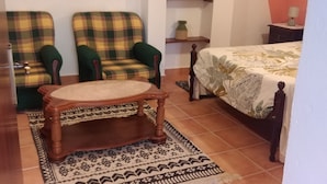 Une pièce avec deux fauteuils à motifs écossais, une table en bois, un lit recouvert d’une couvre-lit à fleurs, un globe terrestre posé sur une étagère et une image d’une grande roue accrochée au mur.