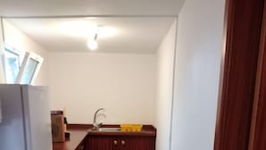 Une cuisine de taille réduite, équipée d’un réfrigérateur, d’un évier et de meubles de rangement en bois.