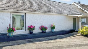 A white building with a grey tiled roof, a window, and three potted plants with flowers.