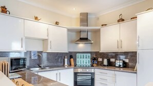 A modern kitchen with white cabinets, a built-in oven, a microwave, and a stainless steel range hood.