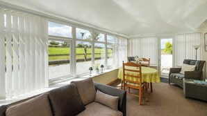 A room with a sofa, dining table, chairs, and a view through large windows.