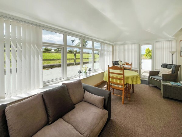 A room with a sofa, dining table, chairs, and a view through large windows.