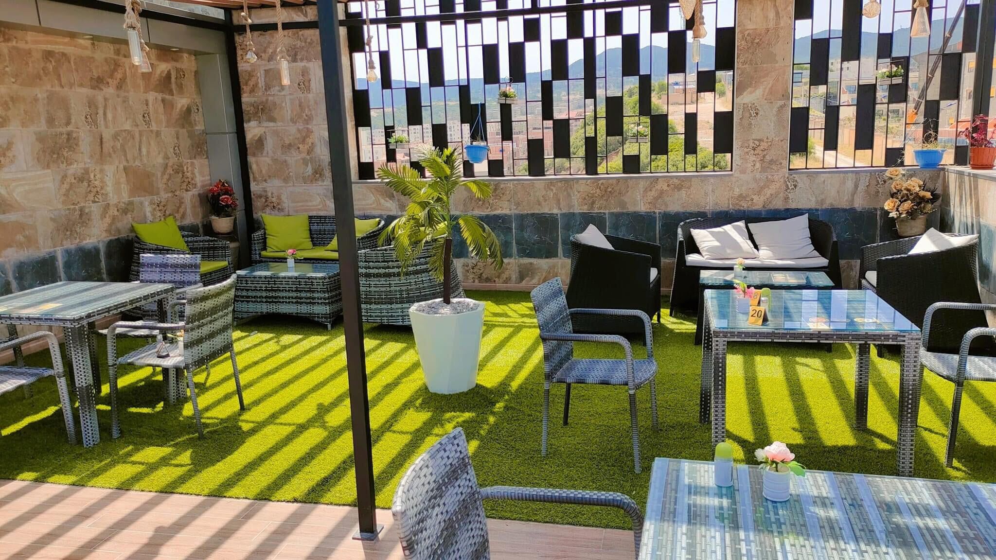 An outdoor patio with wicker furniture, a glass table, and a view of the city through a patterned fence.