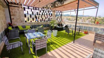 A rooftop patio with outdoor furniture, a grill, and a view of the cityscape.