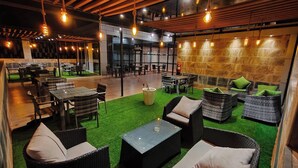 An indoor seating area with wicker furniture and artificial grass, featuring tables and chairs, and a stone wall in the background. - Hotel Boulefkhad (Filfila)