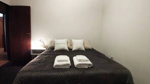 A neatly made bed with a dark patterned bedspread, two pillows with text, and two folded towels. - Duerme Ushuaia Centrico (Ushuaia)