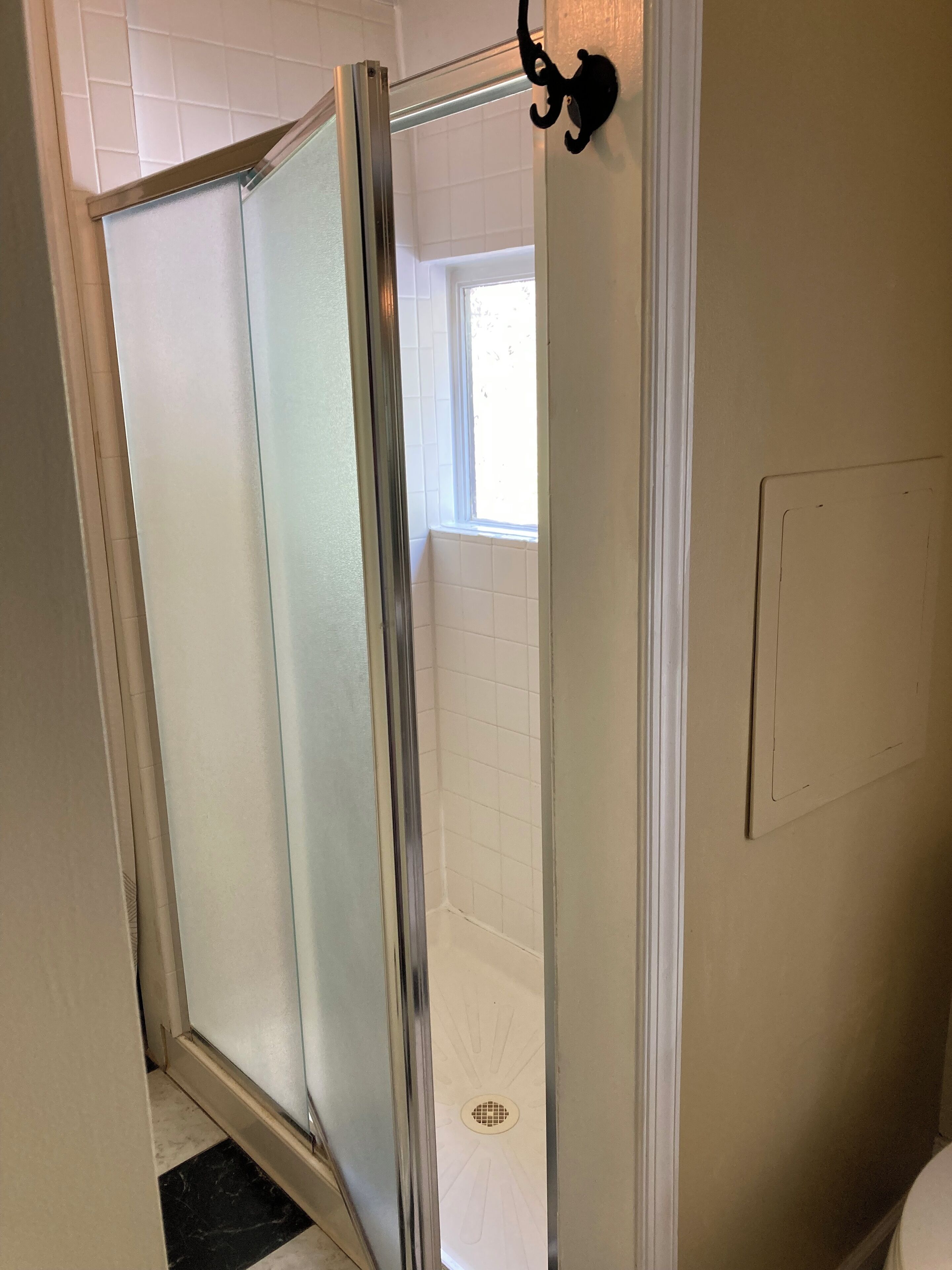 Une salle de bain avec une douche à parois de verre, des murs recouverts de carreaux blancs et une fenêtre.