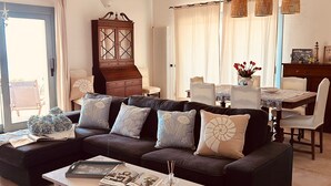 Un salon avec un canapé foncé, une table basse blanche et un coin repas comprenant une table et des chaises.