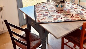 Un coin repas avec une table dressée pour deux personnes, un vase de fleurs et une vue sur la mer par une porte.