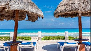 Eine Strandlounge mit Reetdachschirmen und weißen Liegestühlen.
