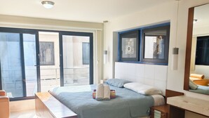 Ein Schlafzimmer mit einem großen Bett, einem Nachttisch, einem Spiegel und Blick durch eine Schiebetür in einen Außenbereich.