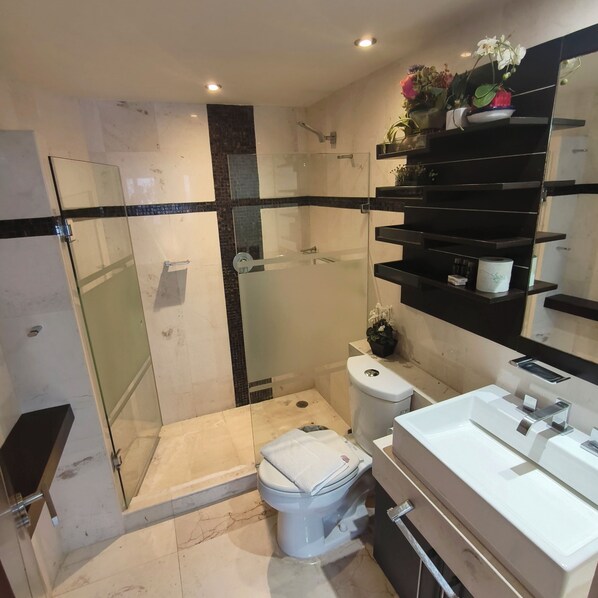 Une salle de bain moderne avec une douche à parois de verre, des toilettes blanches et un meuble-lavabo doté d’un miroir et d’étagères.