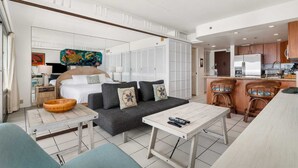 Una habitación de hotel moderna con sofá, una mesita, zona de cocina con refrigerador y comedor con taburetes de bar.