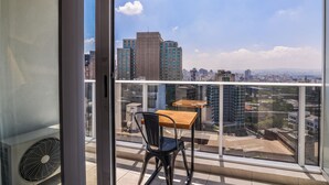 Ein Balkon mit Tisch und Stuhl, mit Blick auf eine Skyline und hohe Gebäude.