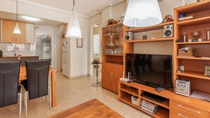 Un salon moderne avec un téléviseur, des étagères en bois et un coin repas avec des chaises.