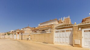 Une rangée de bâtiments beiges, dotés de portails et de balcons blancs, sous un ciel bleu dégagé.