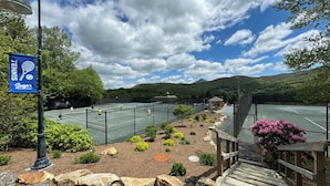 En tennisbana med en banderoll, omgiven av vackert anlagda trädgårdar och med ett bergigt landskap i bakgrunden.