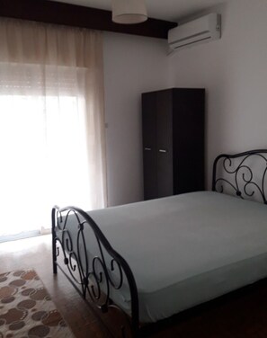 Simple, functional bedroom with a single bed, large window, and air conditioning unit.