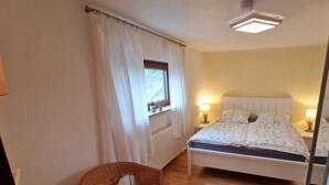 A bedroom with a bed, two bedside lamps, a window with a view, a chair, and a radiator. - Gemütliche Ferienwohnung bei Bernkastel-kues, Ideal zum Wandern und Radfahren (Veldenz)