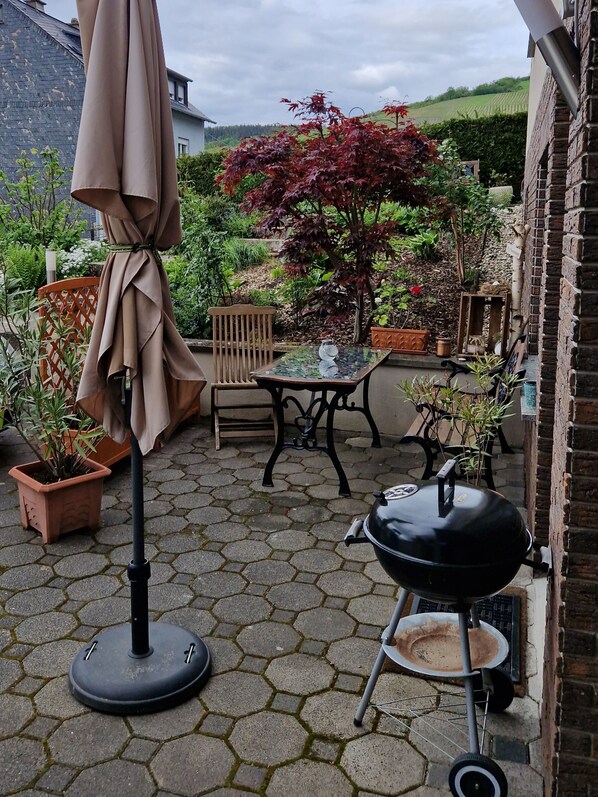 Un patio con una mesa, sillas, una parrilla y plantas en macetas.