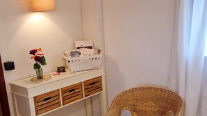 A room with a wicker chair, a white console table with drawers, a small vase with flowers, a lamp, and a basket of books. - Gemütliche Ferienwohnung bei Bernkastel-kues, Ideal zum Wandern und Radfahren (Veldenz)