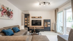 A modern living room with a sofa, a coffee table, and a TV. There is a bookshelf and a cabinet with decorative items. - Apartment Magic Moments (Rijeka)