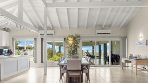 A modern kitchen with a large island, a dining area with a glass table, and a view through large sliding glass doors.