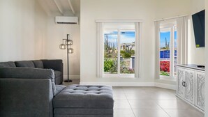 Una sala de estar moderna con un sofá gris, una lámpara de pie y vistas a un jardín a través de amplios ventanales.