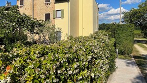 Et toetagers hus med en stenfacade og en gul tilbygning, omgivet af frodigt grønt og en klar himmel.