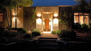 Um edifício moderno com entrada bem iluminada, rodeado por jardins ajardinados e árvores.