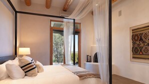 Quarto com uma cama grande, um abajur, uma janela com cortinas leves e uma obra de arte emoldurada na parede.