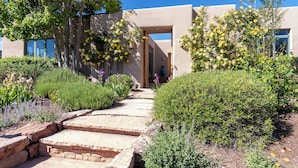 Um caminho leva a um edifício com arquitetura moderna, cercado por vegetação exuberante e plantas floridas.