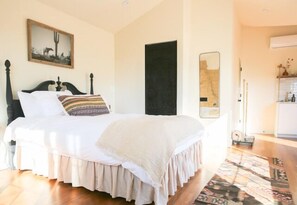 Une chambre avec un lit, une porte, un miroir et une petite kitchenette.