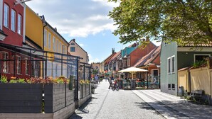 A cobblestone street lined with colorful buildings, outdoor seating areas, and a bicycle parked on the sidewalk.