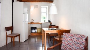 A compact kitchen with a refrigerator, microwave, and sink. There is a dining table with chairs and a patterned cushion.