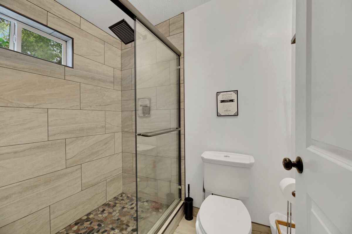Un baño moderno con cabina de ducha de vidrio, inodoro blanco y lavamanos pequeño.