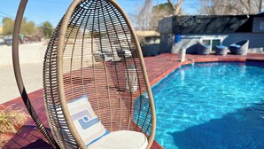 A wicker chair with a cushion by a swimming pool. - Spacious 9-bedroom house in Las Vegas 15 min to The Strip! (Las Vegas)