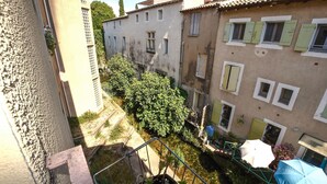 Un stretto vicolo tra edifici, con un piccolo giardino, una recinzione in metallo e un ombrello blu.