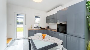 A modern kitchen with grey cabinets, a Bosch oven, and a glass table with fruit. - Beautiful home in Maslenica with WiFi (Maslenica)