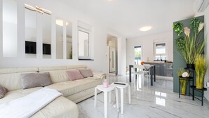 A modern living room with a beige sofa, white coffee table, and a kitchen area with a dining table and chairs. - Beautiful home in Maslenica with WiFi (Maslenica)