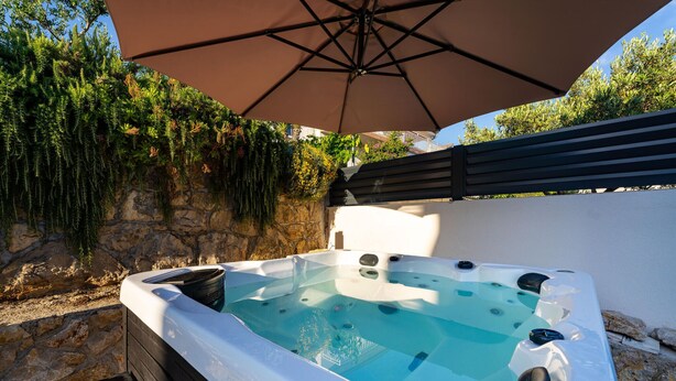 A hot tub with a stone wall backdrop, an umbrella, and lush greenery. - Beautiful home in Maslenica with WiFi (Maslenica)