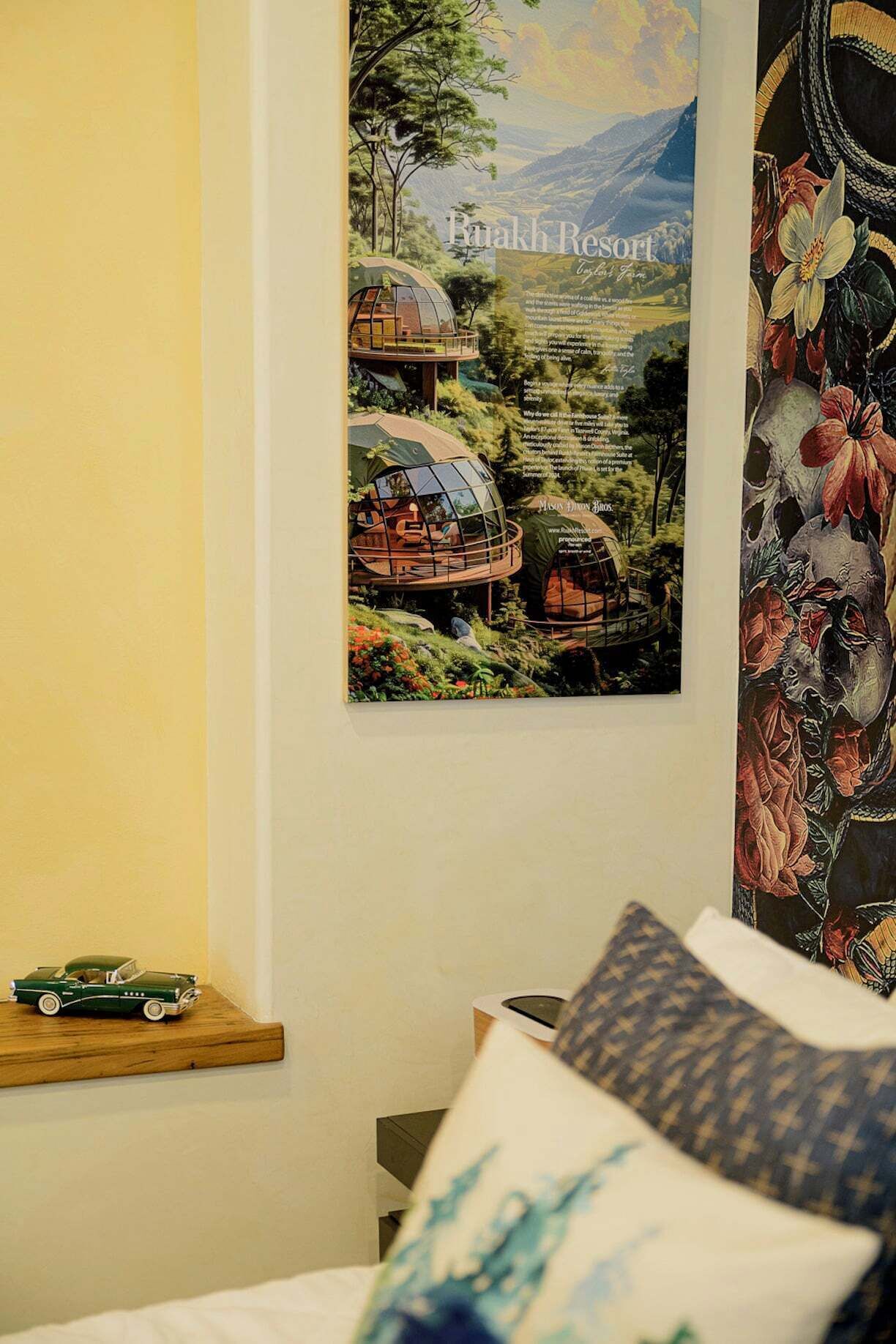A bedroom with a bed, pillows, a small wooden shelf with a model car, and a poster of a resort.
