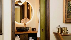 Une salle de bain avec un meuble-lavabo en bois, un miroir rond, un évier et un porte-serviettes.
