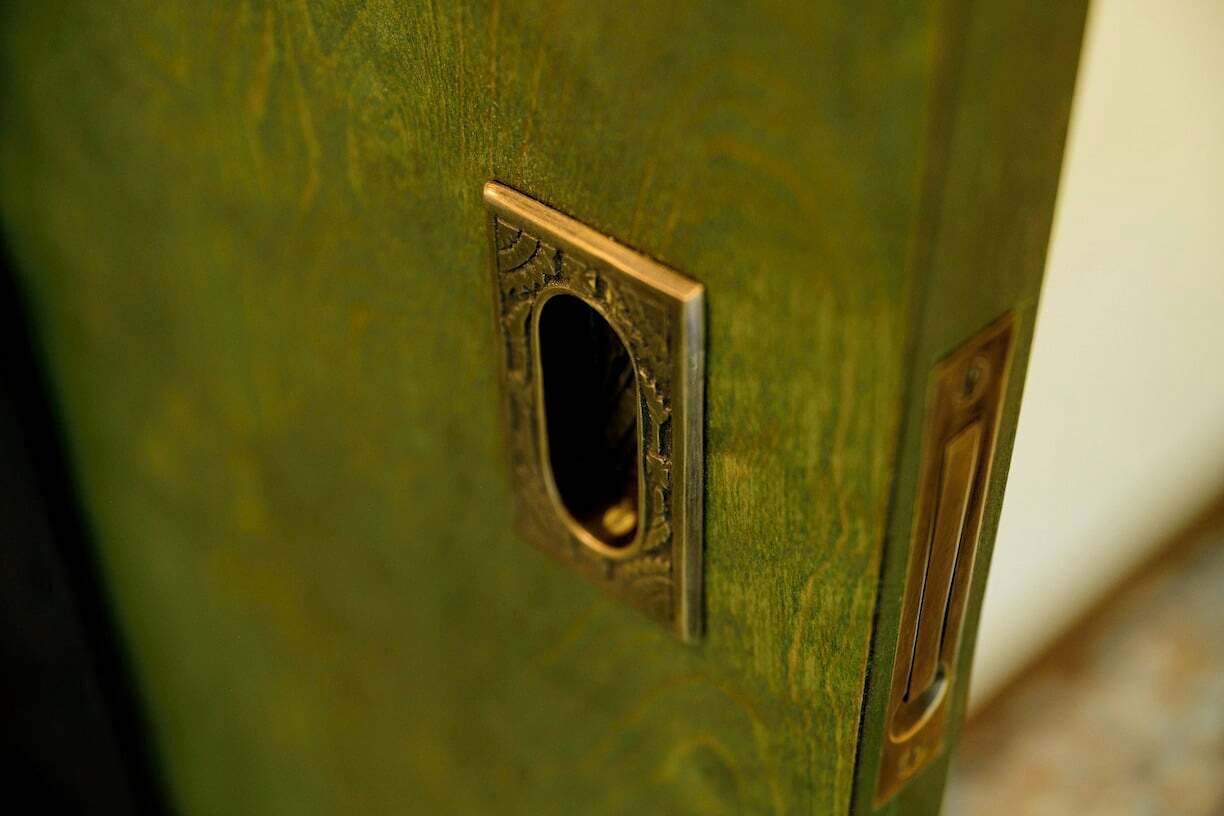 Un primer plano de una puerta de madera con picaporte de latón y una pequeña ventana rectangular.